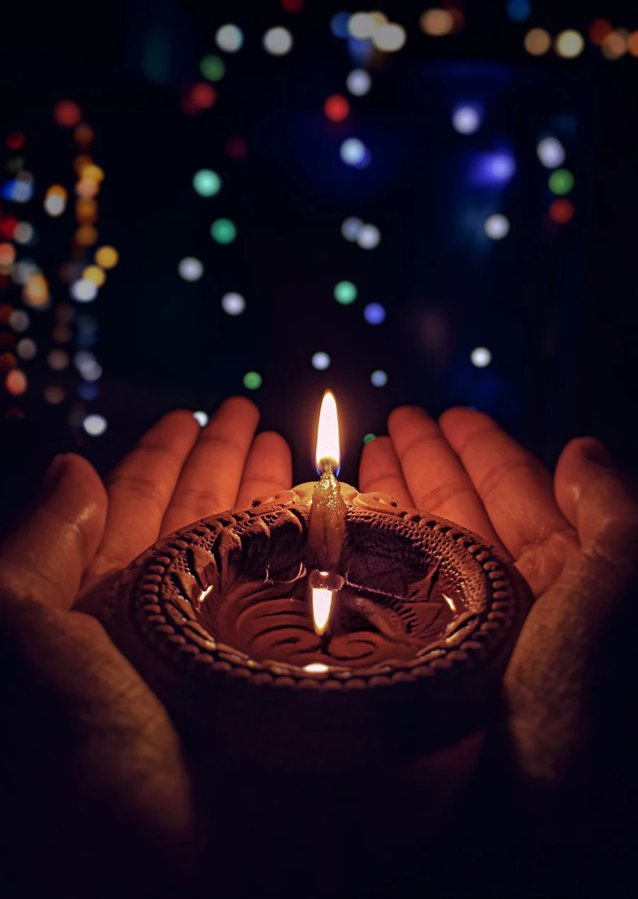 A lit diya held in cupped hands, in memory of Bhartiben Sanghadia